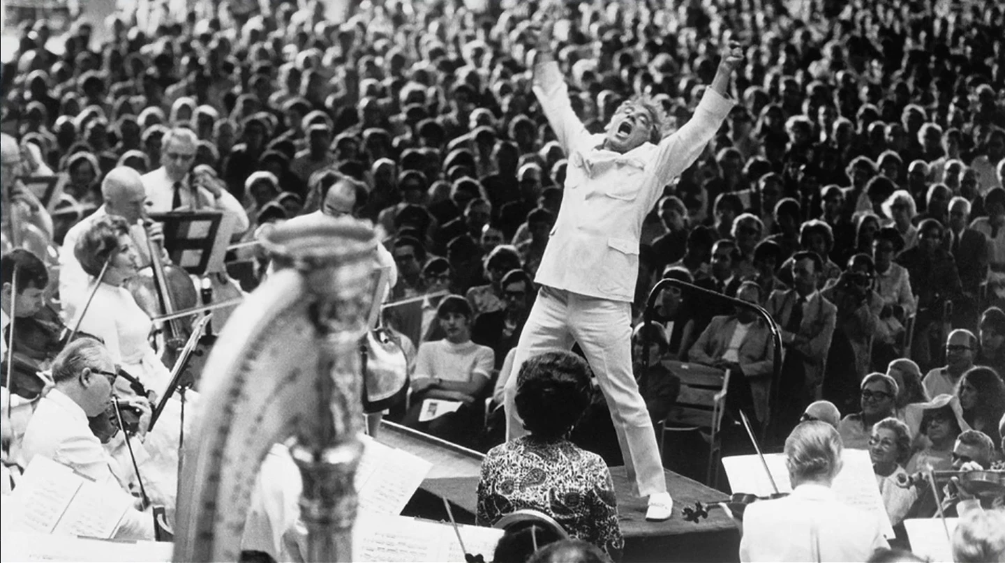 Black-and-white photograph of a conductor leading an orchestra before an audience.